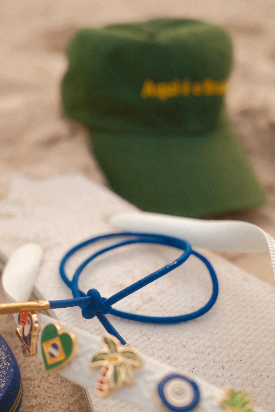 Blue Loopi hair tie resting on a flip-flop in the sand